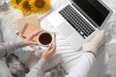 Bir fincan kahvesi, bilgisayarı, ayçiçekleri ve defterleri olan bir kadın.