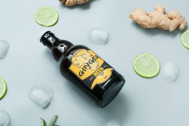 Gri arkaplanda taze zencefilli bira, limon dilimleri ve buz küpleriyle kompozisyon, yakın plan.