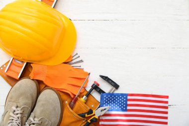 Koruyucu teçhizat, aletli kemer ve beyaz ahşap arka planda Amerikan bayrağı. İşçi Bayramı kutlamaları