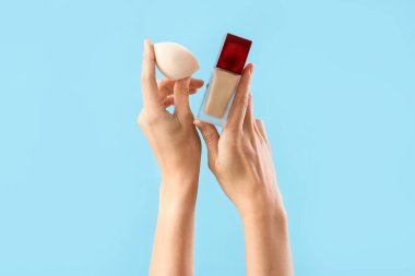 Makyaj temeli ve süngeri mavi arka planda olan kadın.