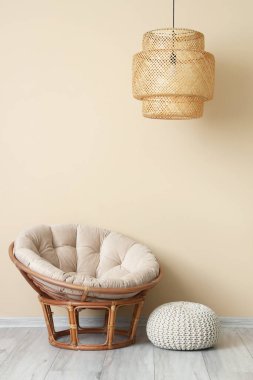 Şık koltuk, hasır lamba ve bej duvarın yanında puf.