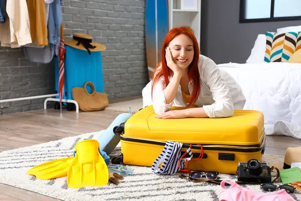 Young woman with packed suitcase in bedroom