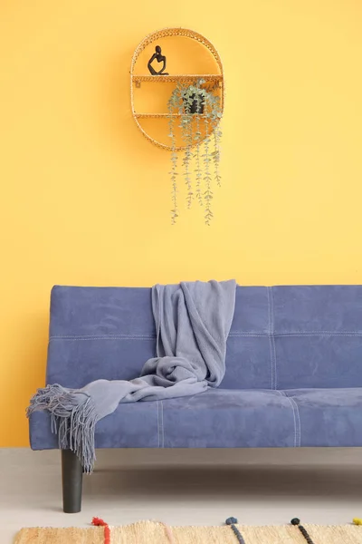 Stylish blue sofa with blanket near orange wall