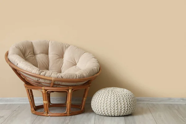 Stylish armchair and pouf near beige wall