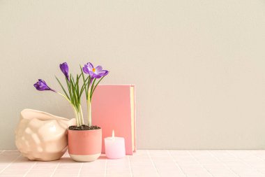 Güzel çiçekli tencere, dekoratif deniz kabuğu, kitap ve yanan mum beyaz duvarın yanındaki masada.