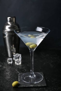 Koyu arkaplanda zeytin ve sallanan bir bardak lezzetli martini.