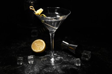 Lezzetli bir bardak martini, buz küpleri, limon ve arka planda ölçü kabı.