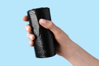 Mavi arka planda çöp torbası rulosu tutan kadın.