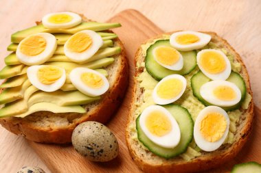Hafif ahşap arka planda bıldırcın yumurtası, avokado ve salatalıklı lezzetli tostlar, yakın plan.