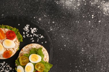 Üzerinde bıldırcın yumurtası, domates ve marul olan pirinç krakerleri.