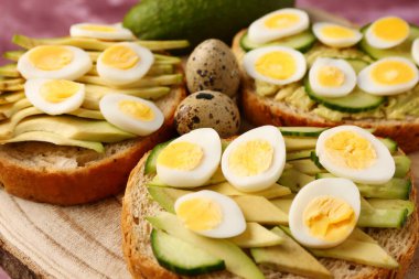 Bıldırcın yumurtalı lezzetli tostlar, avokado ve salatalık masada, yakın plan.