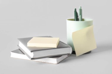 Gri arkaplan üzerine yapışkan notları ve kitapları olan kalem tutucu