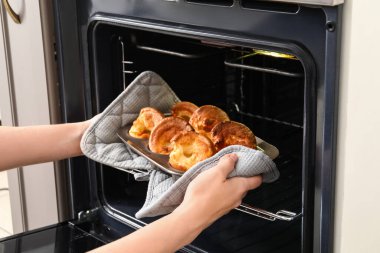 Mutfaktaki fırından lezzetli Yorkshire pudingiyle yemek pişiren kadın.
