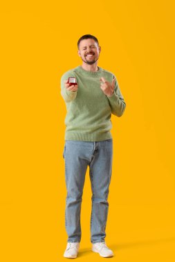 Nişan yüzüklü genç adam sarı arka planda şans diliyor.