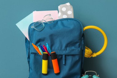 Mavi arka planda farklı kırtasiye malzemesi ve kulaklık olan okul çantası.