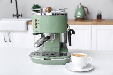 Modern coffee machine with cup of hot espresso on table in kitchen