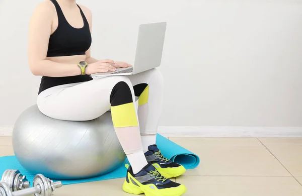 Sporty woman using laptop on fitball in gym