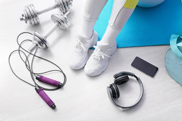 Woman with sports equipment, headphones and mobile phone on white wooden floor, closeup