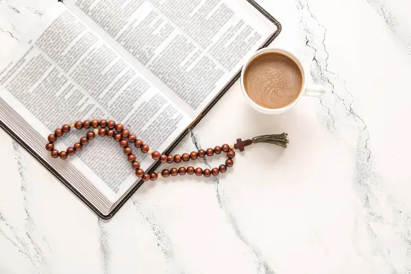 Holy Bible with cup of coffee and prayer beads on grunge white background