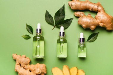 Bir şişe zencefil kozmetik yağı ve yeşil arka planda yapraklar