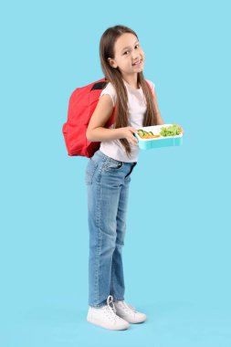 Sırt çantası ve mavi arka planda beslenme çantası olan mutlu küçük kız.