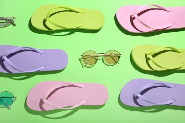 Yeşil arka planda renkli terlik ve güneş gözlüğü.