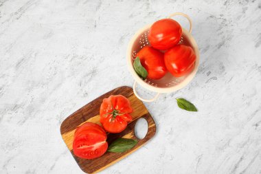 Tahta tahta ve taze olgun domateslerden oluşan bir kevgir ve beyaz arka planda fesleğen.
