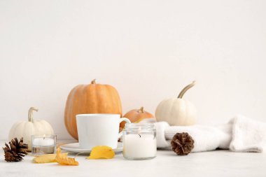 Bir fincan çay, sonbahar yaprakları, kazak, yanan mumlar, kozalaklar ve beyaz arka planda balkabakları.