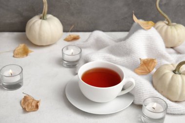 Bir fincan çay, yanan mumlar, kazak, balkabağı ve sonbahar yaprakları masada.