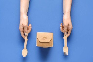 Paketlenmiş kağıt kutusu ve mavi arka planda çatal bıçak takımı olan kadın eller.
