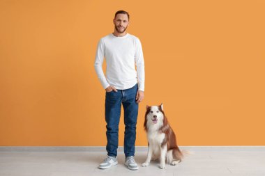 Turuncu duvarın yanında sevimli köpekli yakışıklı bir genç.