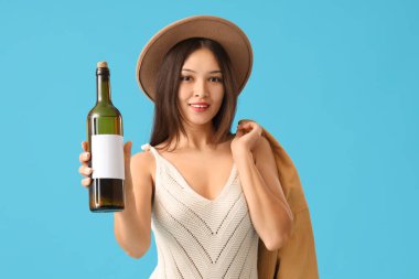 Mavi arka planda şarap şişesi olan genç Asyalı kadın.