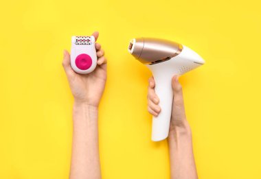 Sarı arka planda modern fotoepilatör ve epilatorlu kadın elleri, yakın plan.