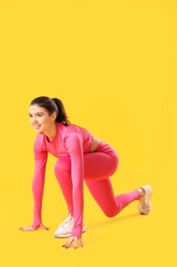 Spor kıyafetli genç bir kadın sarı arka planda koşmaya hazırlanıyor.