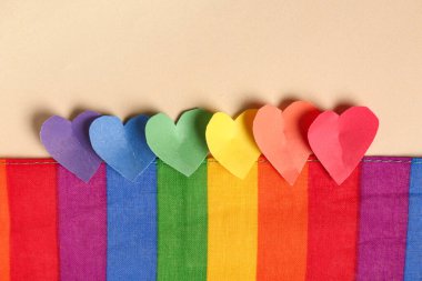 Renkli arka planda gökkuşağı bayrağı ve renkli kağıt kalplerle kompozisyon, yakın plan. Sevgililer Günü kutlaması