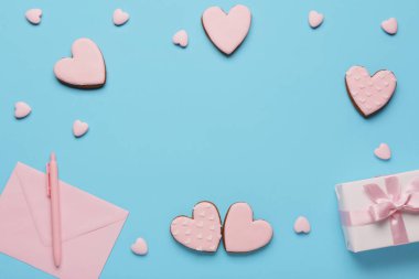 Kalp şeklinde kurabiyelerden yapılmış çerçeve. Hediye kutusu ve mavi arka planda zarf var. Sevgililer Günü kutlaması