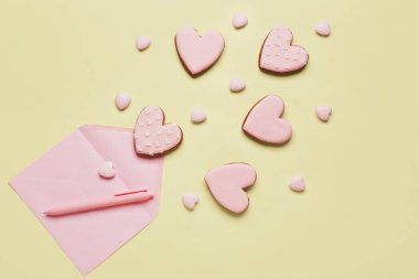 Kalp şeklinde tatlı kurabiyeler ve sarı arka planda bir zarf. Sevgililer Günü kutlaması