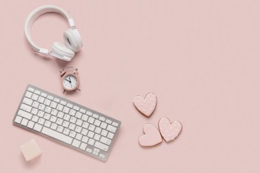Kalp şeklinde klavyeli kurabiyeler, kulaklıklar ve pembe arka planda çalar saat. Sevgililer Günü kutlaması