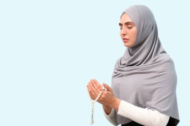 Boncuklu genç Müslüman kadın açık mavi arka planda dua ediyor