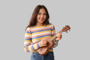 Gri arka planda ukulele çalan genç kadın.