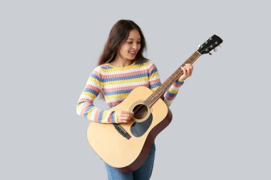 Gri arka planda gitar çalan genç bir kadın