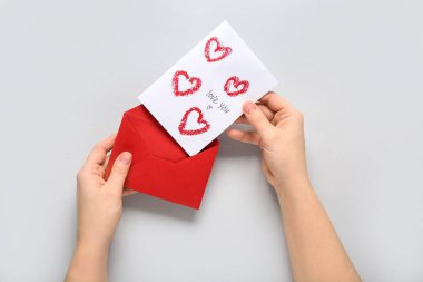 Kırmızı zarflı kadın eller ve gri arka planda tebrik kartı, yakın plan. Sevgililer Günü kutlaması