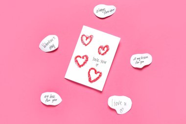 Tebrik kartı ve pembe arka planda ilan-ı aşk yazılı kağıt parçaları. Sevgililer Günü kutlaması