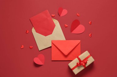 Zarflı kompozisyon, boş kart, kağıt kalp ve kırmızı arka planda hediye kutusu. Sevgililer Günü kutlaması