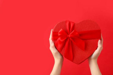 Kırmızı arka planda kalp şeklinde hediye kutusu olan kadın elleri. Sevgililer Günü kutlaması