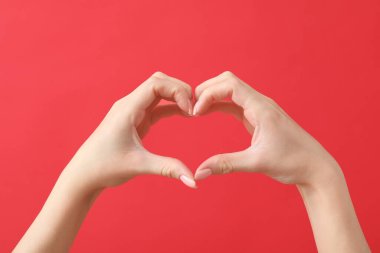 Kırmızı arka planda kalp hareketi gösteren kadın elleri. Sevgililer Günü kutlaması