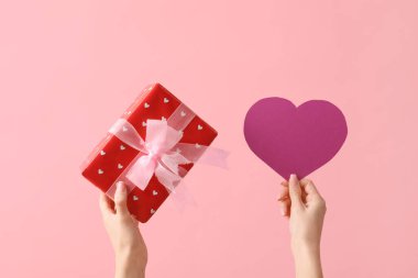 Kağıt kalpli kadın eller ve pembe arka planda hediye kutusu. Sevgililer Günü kutlaması