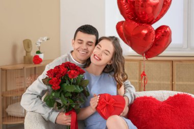 Young couple with bouquet of roses and gift for Valentine's day at home