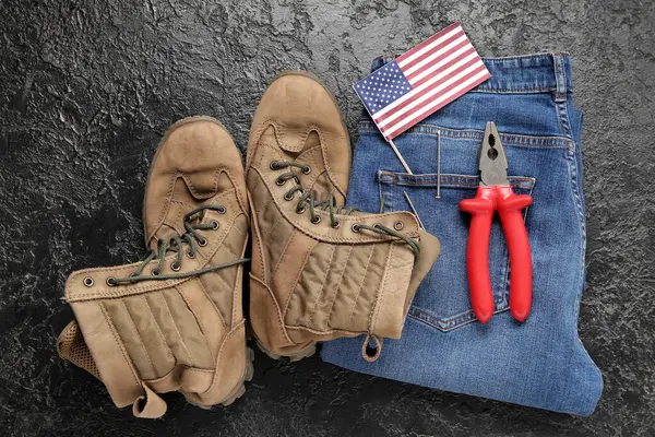 Pair of work boots, USA flag, jeans and pliers on black background. Labor Day celebration