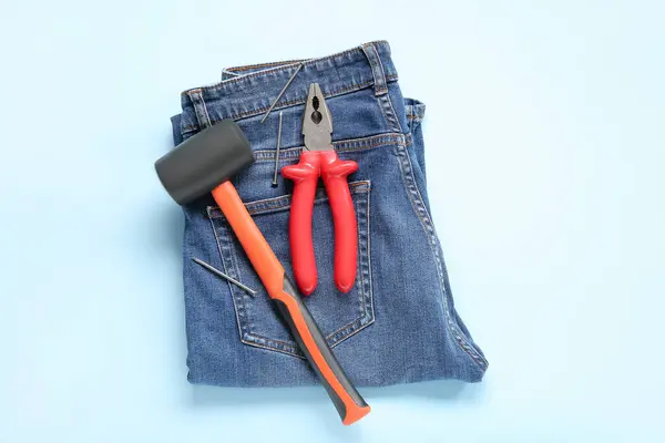 Jeans with rubber mallet and pliers on blue background. Labor Day celebration